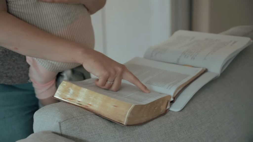 Mom holding a baby in a wrap style carrier while reading the Bible.